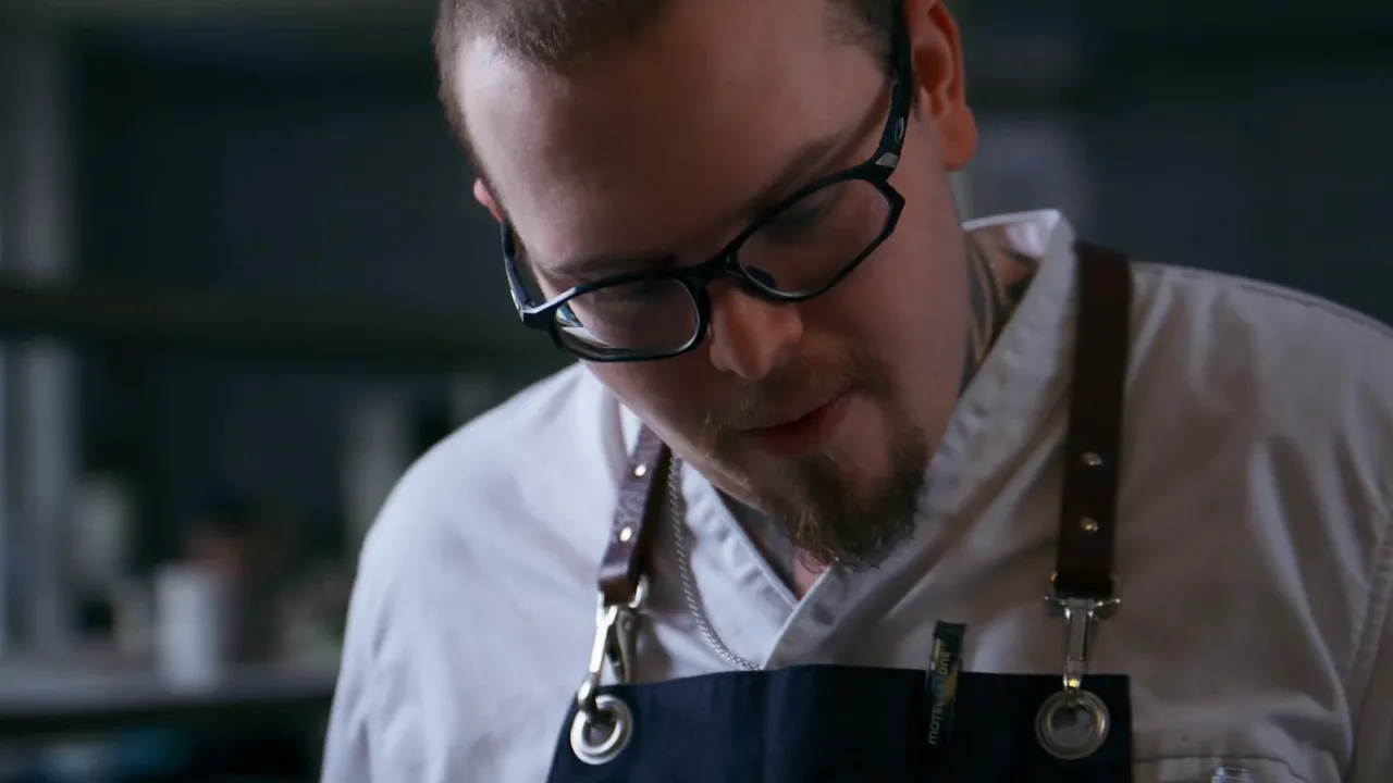 Junger Koch mit Brille und Schürze konzentriert bei der Arbeit in der Küche